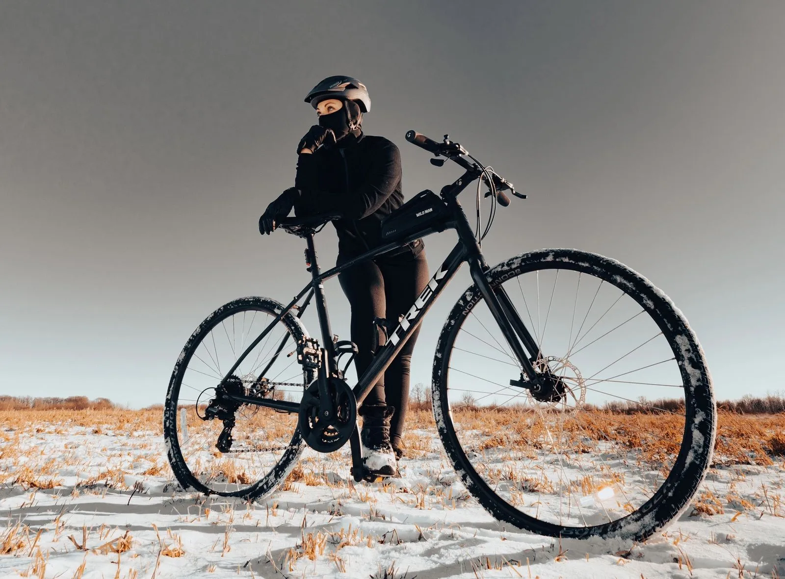 Bicyclist standing with mountain bike on a snow-covered field during winter season.