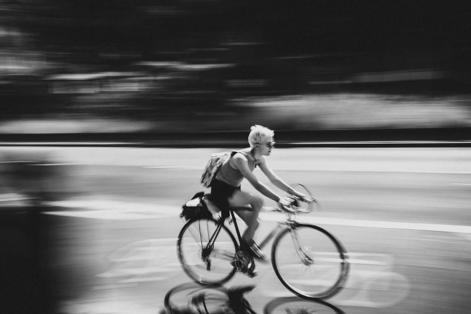 Black and white photo of cyclist creating motion blur effect on city street.